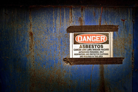 Sign warns workers of asbestos danger and promotes protective clothing.
