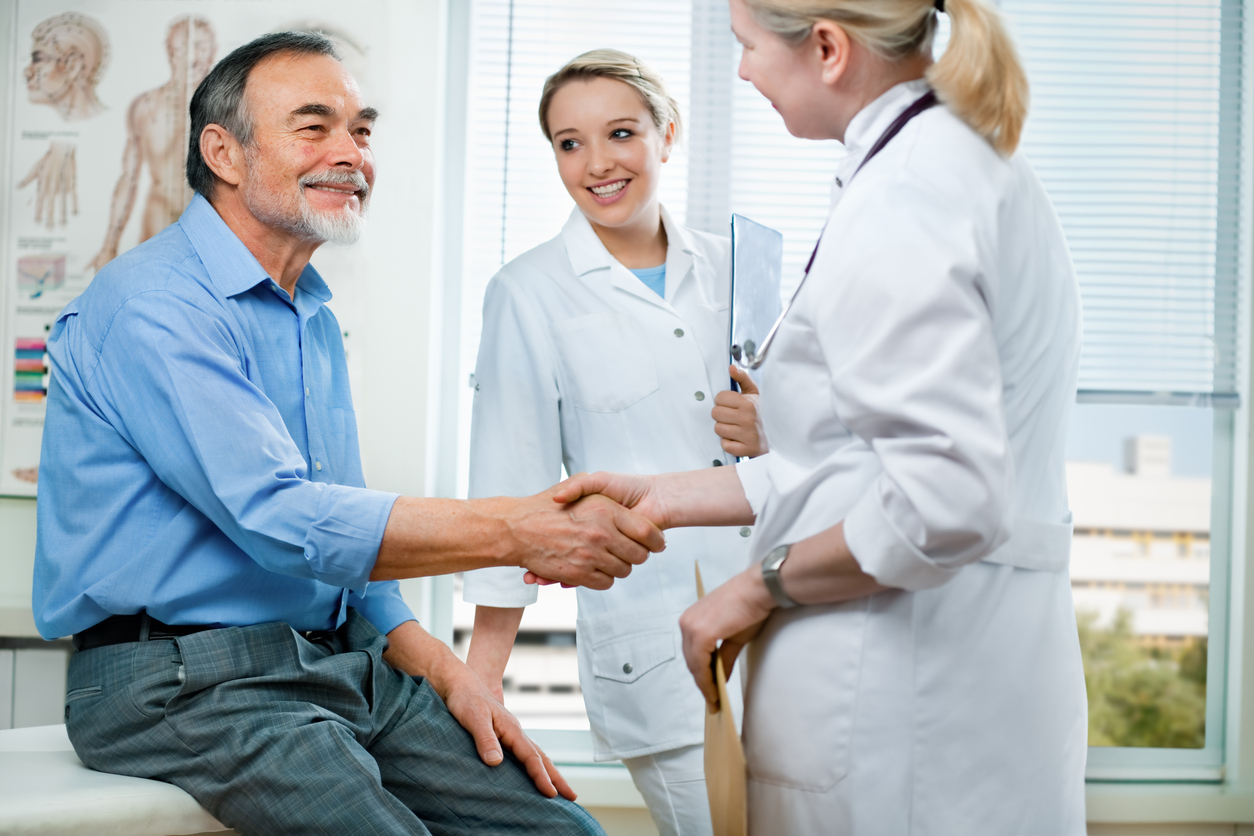 Male patient shaking hands with a female doctor, while another doctor smiles.